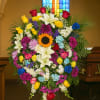 Large colorful funeral spray with roses, lilies, and a sunflower on an easel