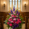Large pink and purple floral arrangement in a church aisle