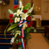 Standing floral spray with white lilies, red carnations, and a red-white-blue ribbon
