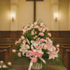 Pink lilies and carnations arranged in a church setting with a ribbon bow