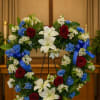 Heart-shaped floral wreath with red roses, white lilies, and blue accents on an easel