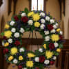 Circular funeral wreath of red, yellow, and white flowers on an easel