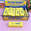 Box of yellow butter-shaped squishy toys on a pink surface