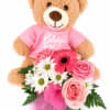 Teddy bear in a pink shirt holding pink and white flowers in a box