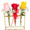 Three roses in glass tubes on a gold stand, with a red ribbon on the center stem