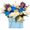 Blue box arrangement with white, purple, and blue flowers and a gold ribbon