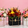 Three floral arrangements in handbag-shaped boxes on a pink background.