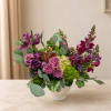 Purple and pink mixed flower arrangement in a white vase