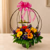 Colorful flower arrangement in a black container with a pink ribbon bow and bird cage topper