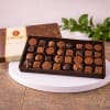 Box of assorted chocolates on a white stand with a decorative box behind it