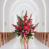 Tall pink floral arrangement with a ribbon in a church aisle