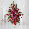 Tall pink and red floral arrangement on a stand in a white interior