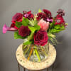 Bouquet of red roses, burgundy blooms, and a pink protea in a glass vase