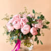 Pink peonies in a clear glass vase with greenery and a magenta ribbon