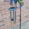 Wind chime with blue ribbon and greenery on a black metal stand