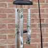 Black metal wind chime with silver tubes and bird designs hanging on a brick wall.