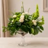 White roses in a clear pedestal vase with lush green foliage