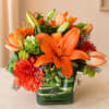 Orange lilies and dahlias in a green striped glass vase