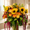 Bouquet of yellow sunflowers and orange-tipped roses in a clear glass vase