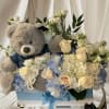 Teddy bear in a box with white and blue flowers