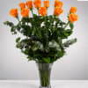 Orange roses arranged in a clear glass vase with mixed greenery