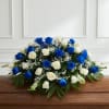 A dense, casket spray of vivid blue and creamy white roses creates