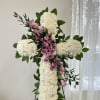 White floral cross with pink roses and greenery on a stand