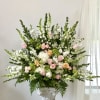 Large floral arrangement with pink and peach roses, white blooms, and greenery in a pedestal vase