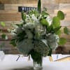 White floral arrangement in a clear glass vase with green foliage