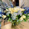 Large bouquet of cream roses, blue flowers, and hydrangeas in a glass vase