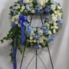 Blue and white floral wreath on a black easel with a purple ribbon