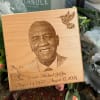 Wooden memorial plaque with a portrait and engraved dates, surrounded by flowers
