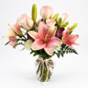 Pink lilies and roses in a glass vase with a ribbon