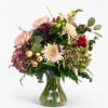 Mixed bouquet of pink, cream, and burgundy flowers in a clear glass vase