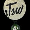 Round white floral tribute with black lettering and ribbon, mounted above a small floral base