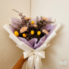 Handheld bouquet of yellow tulips and pale flowers wrapped in lavender and white paper