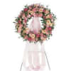 Pink and peach floral wreath on a white stand with a sheer ribbon