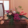 Tropical floral arrangement with pink anthuriums and protea on a wooden casket