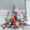 Tall mixed floral arrangement in a white container with bright multicolored blooms
