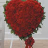 Heart-shaped red floral arrangement on a white stand with a red ribbon