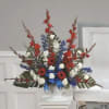 Tall red, white, and blue floral arrangement in a white pedestal vase
