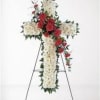 Cross-shaped floral funeral spray with white flowers and red roses on a stand