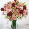 Bouquet of red roses, pink lilies, and white daisies in a glass vase