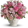 Pink roses and lilies arranged in a white pedestal vase