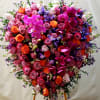Heart-shaped floral arrangement with pink roses, orchids, and purple flowers