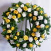 Yellow roses and white carnations arranged in a circular wreath on an easel