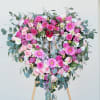 Heart-shaped floral wreath of pink roses and daisies on a wooden stand