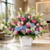Large mixed flower arrangement in a white vase with pink, blue, and white blooms