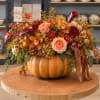 Autumn floral arrangement in a pumpkin container with roses and orchids