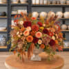 Autumn floral arrangement in a stone urn with orange, red, and peach blooms